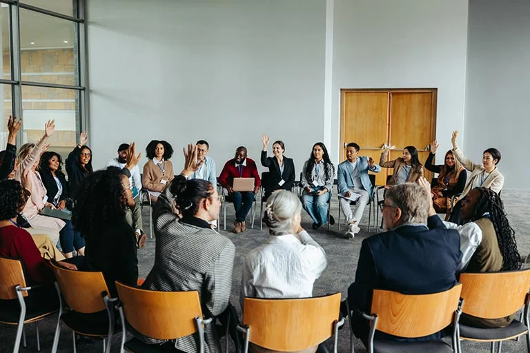 Menschen sitzen im Stuhlkreis, viele heben die Hand
