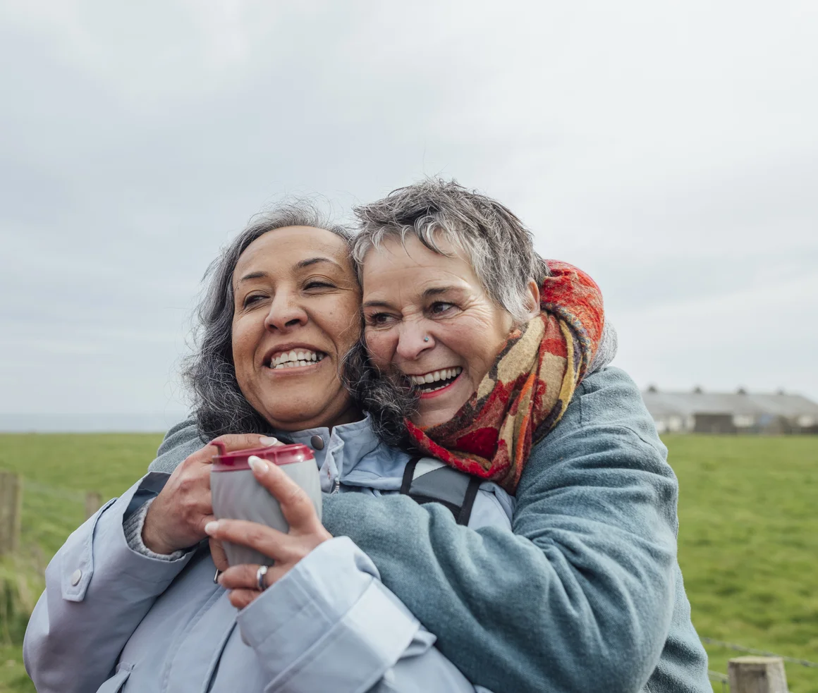 Zwei Frauen umarmen sich herzlich und lachend in der Natur