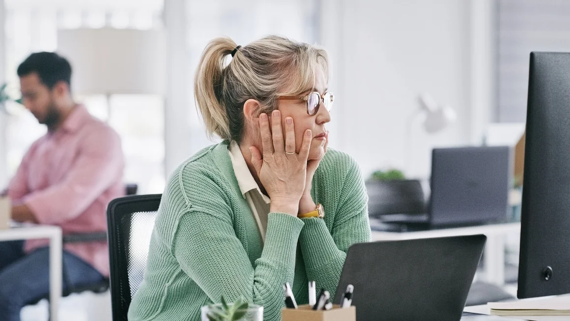 Erschöpfte Frau sitzt am Arbeitsplatz vor einem Laptop